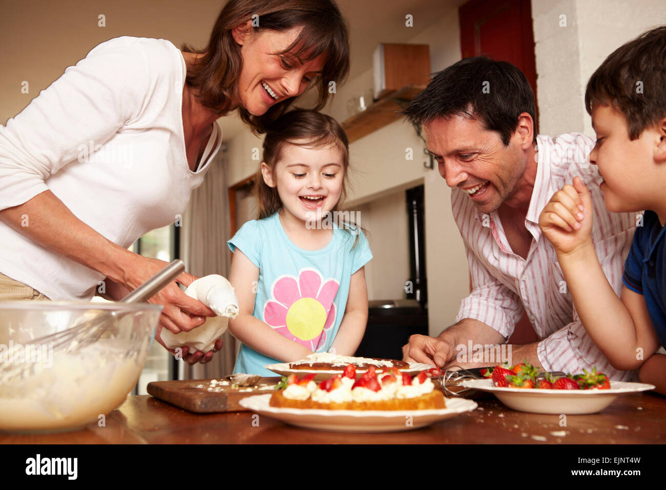Eine Familie, zwei Eltern und zwei Kinder in der Küche einen Kuchen mit Obst und Sahne Puderzucker. Stockfoto