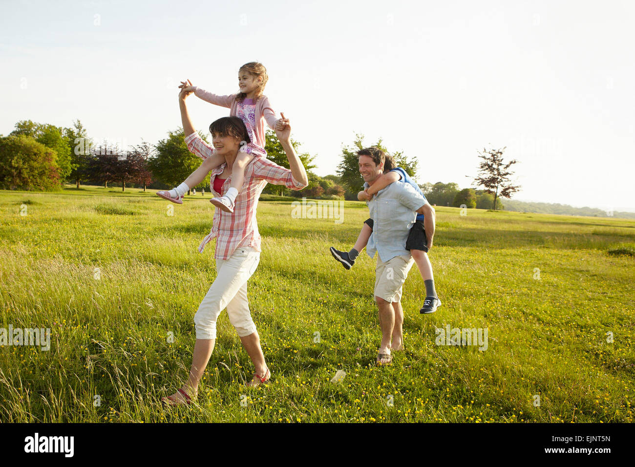Eine Familie, zwei Eltern im Freien im Sommer geben piggybacks für zwei Kinder. Stockfoto