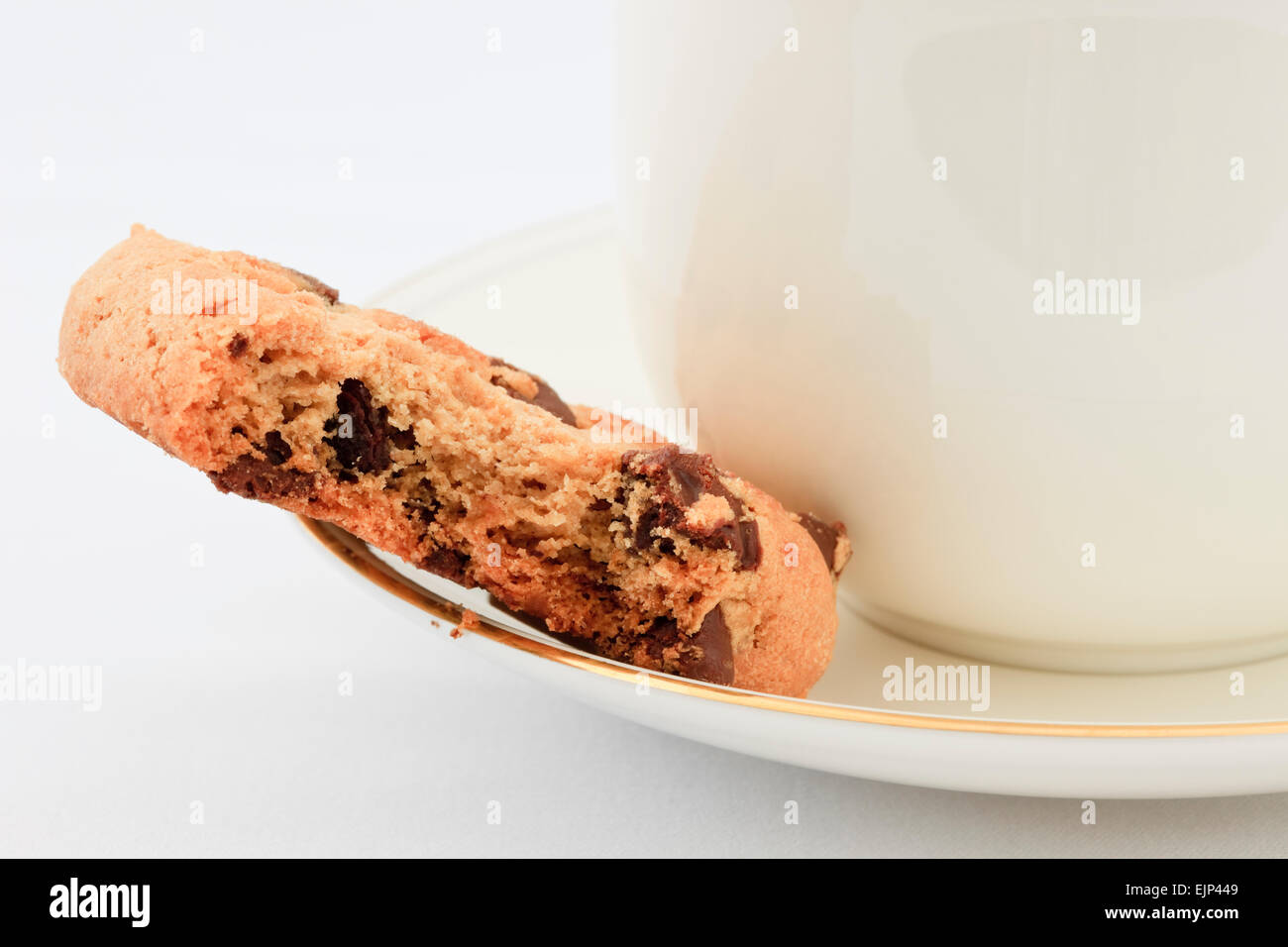 Chocolate Chip Keks mit einem Biss auf der Untertasse mit einer Tasse englischen Tee herausgenommen. England, UK, Großbritannien Stockfoto