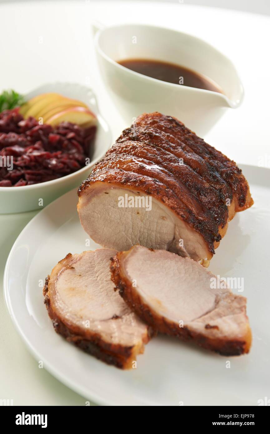 Braten Sie Sonntag Schwein Mittagessen Sauciere Rotkohl Apfelscheiben knisternde Runde weiße Platte Stockfoto