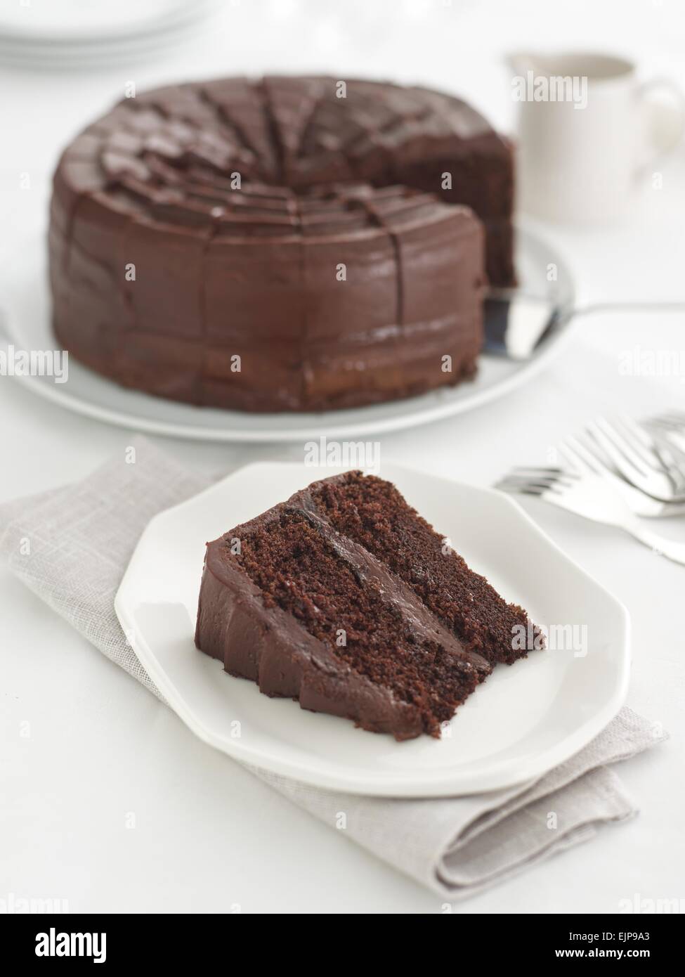 Schokoladen-Kuchen mit Zuckerguss und ein Stück entfernt von ihm auf einem Teller Stockfoto