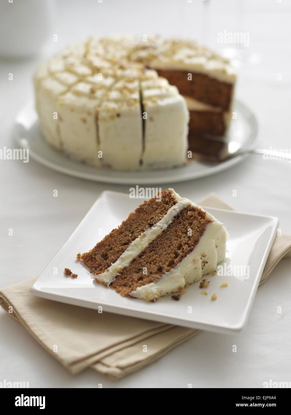 Walnuss-Kuchen mit weißer Glasur und ein Stück entfernt von ihm auf einem Teller Stockfoto
