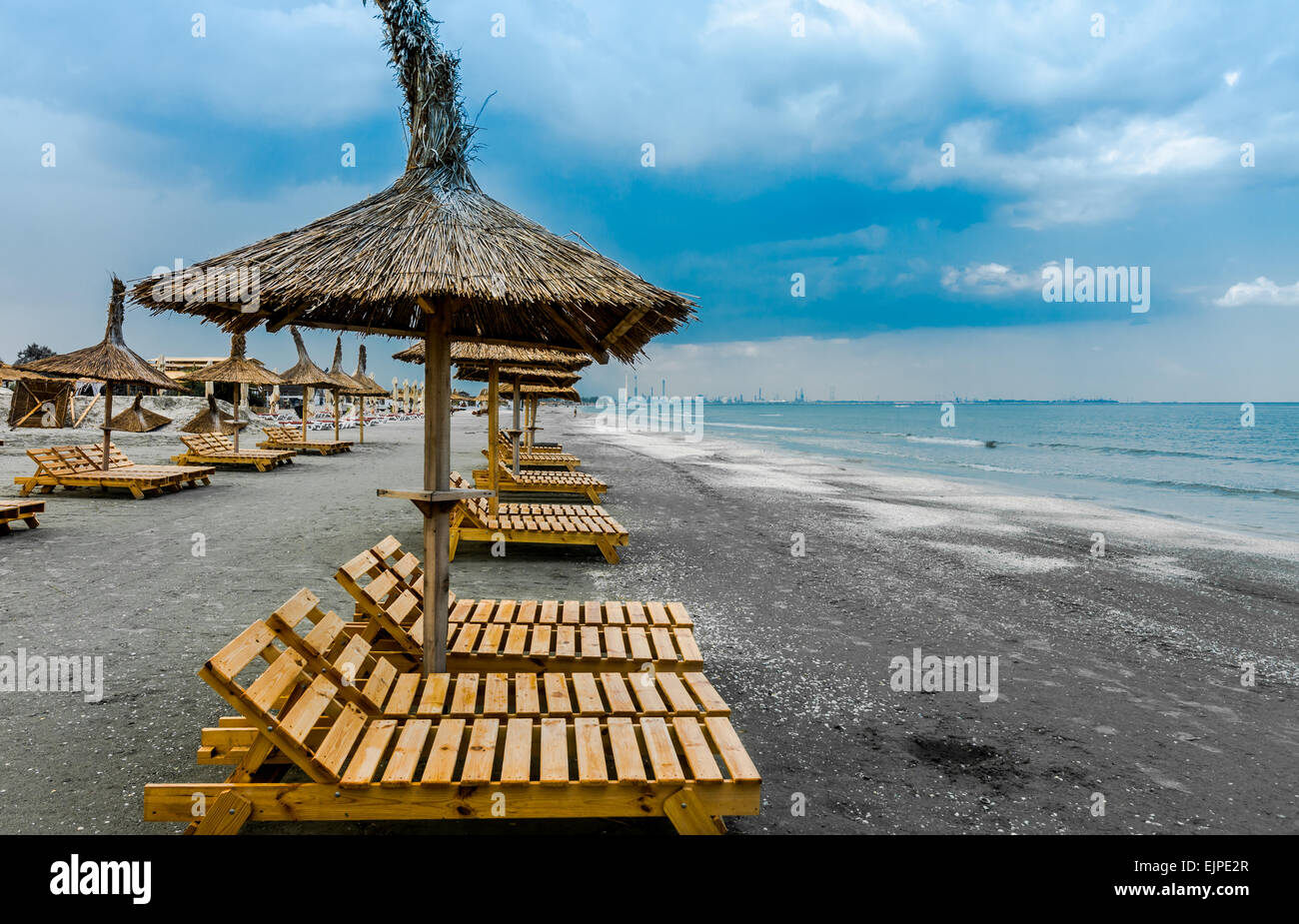 Trübe Meer Strand mit liegen aus Holz und Stroh Sonnenschirme. Stockfoto