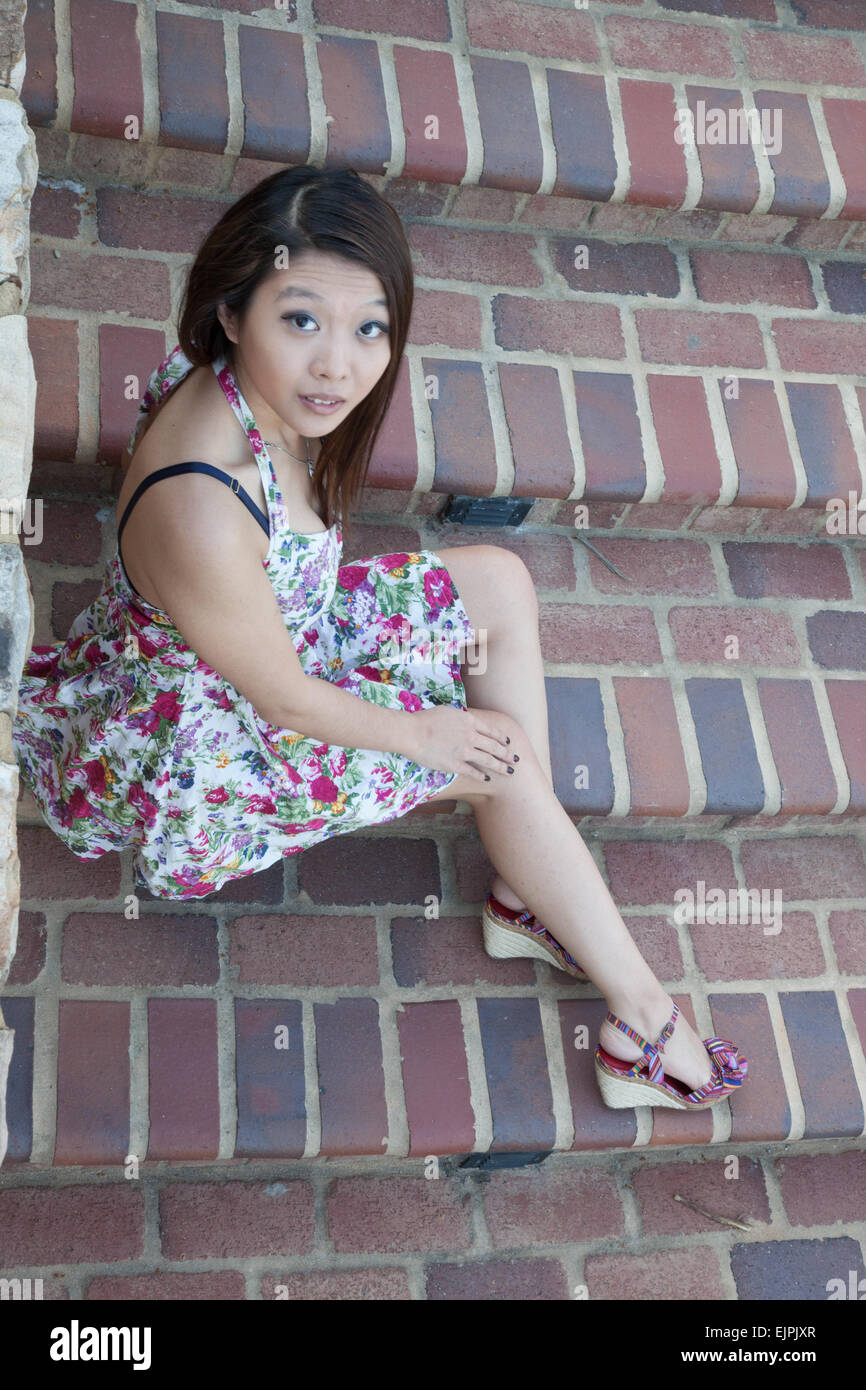 Ziemlich Asian Frau sitzen auf Stufen im Freien in einem geblümten Kleid, nachdenklich Stockfoto