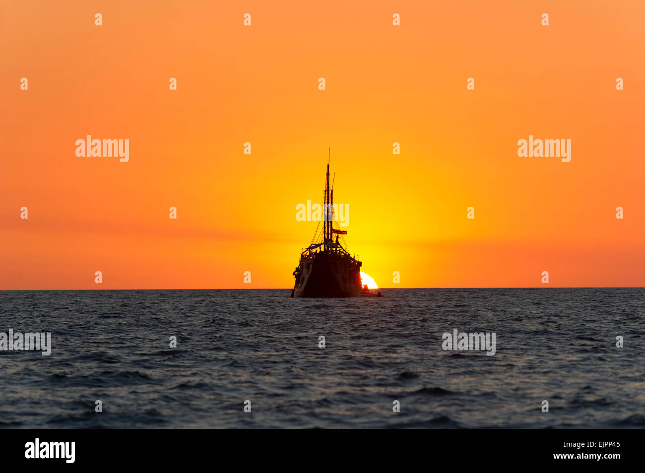 Ein altes Holzschiff befindet sich am Meer und beobachtet die Fantasie Sonnenuntergang im Hintergrund. Stockfoto