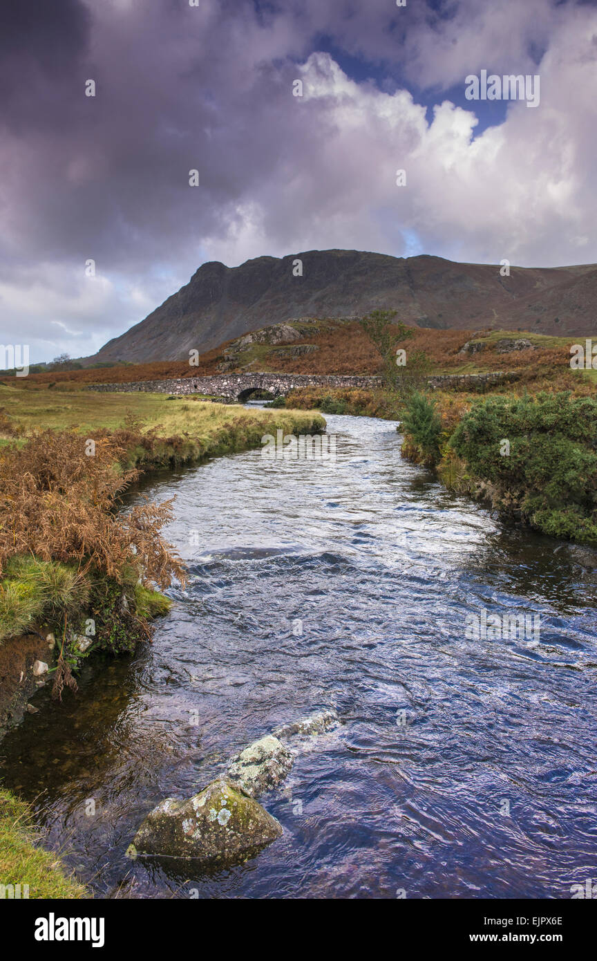 Blick auf Fluss und Brücke im Hochtal, mit Seatallan Peak im Hintergrund, Overbeck Brücke über Beck, in der Nähe von Wastwater, tiefste, Lake District Nationalpark, Cumbria, England, Oktober Stockfoto