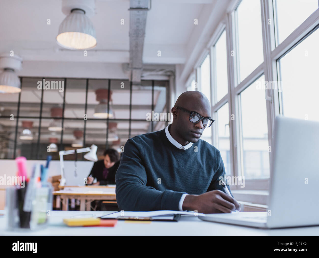 Afrikanischer Mann schreiben von Notizen während der Arbeit auf einem Laptop in einem modernen Büro. Beschäftigt junge Mann arbeitet an seinem Schreibtisch. Stockfoto