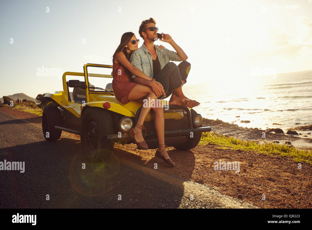 Porträt des jungen Paares sitzen auf einem ihr Auto am Meeresufer, mit Mann mit Handy. Paar auf Sommerurlaub. Stockfoto