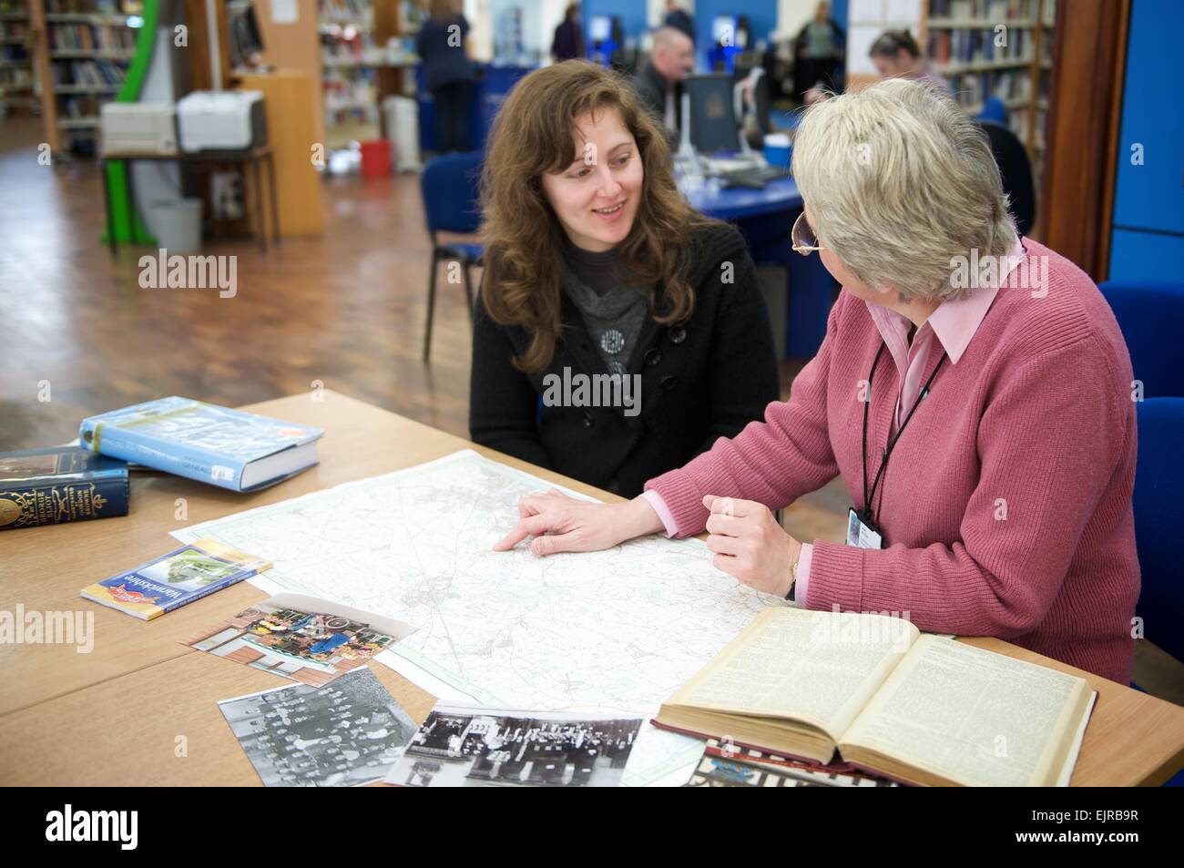 Junge Frau lernt etwas über ihre Familiengeschichte von Forscher an einer öffentlichen Bibliothek Stockfoto