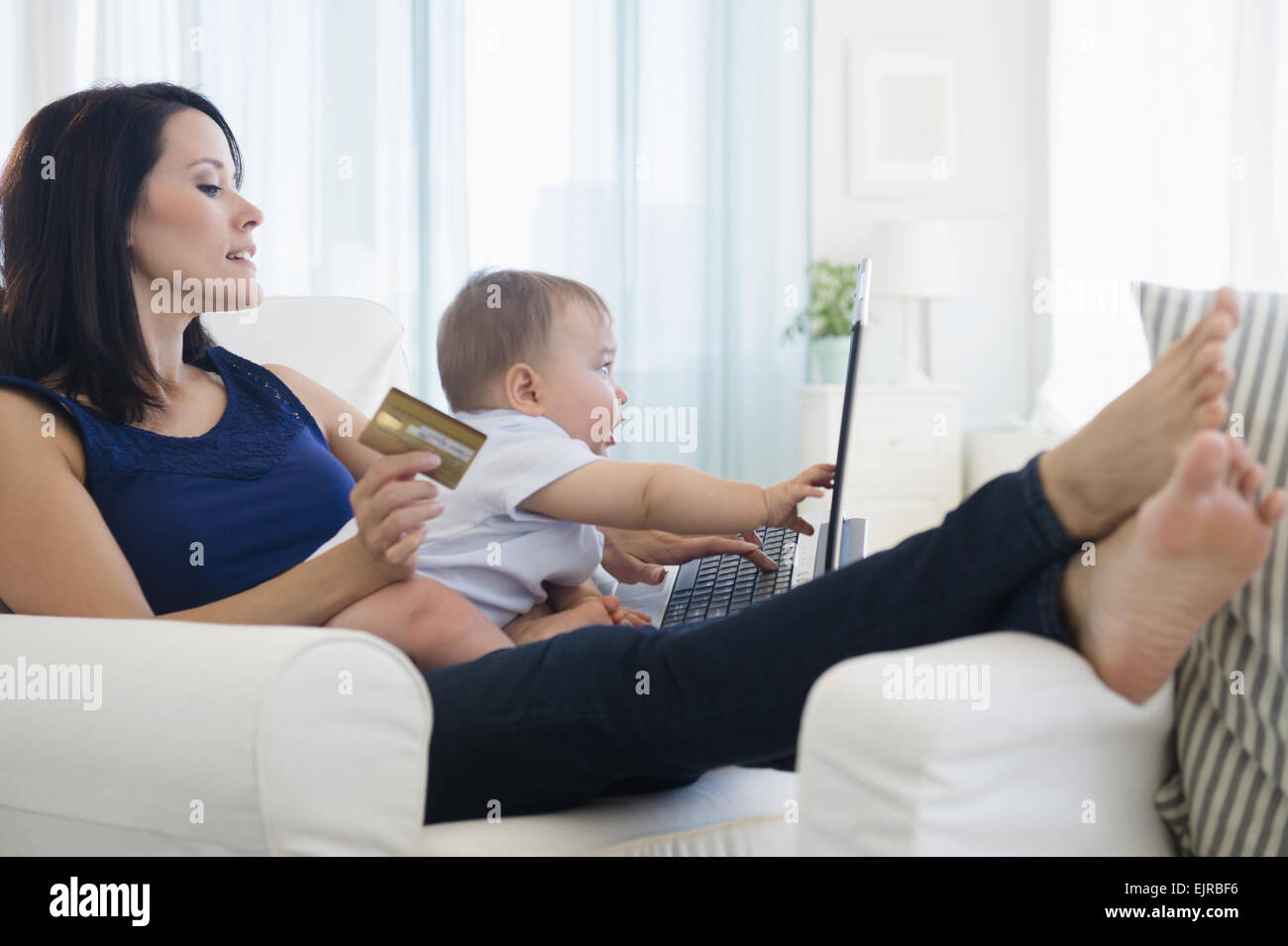 Mischlinge Mutter hält Baby und shopping auf laptop Stockfoto