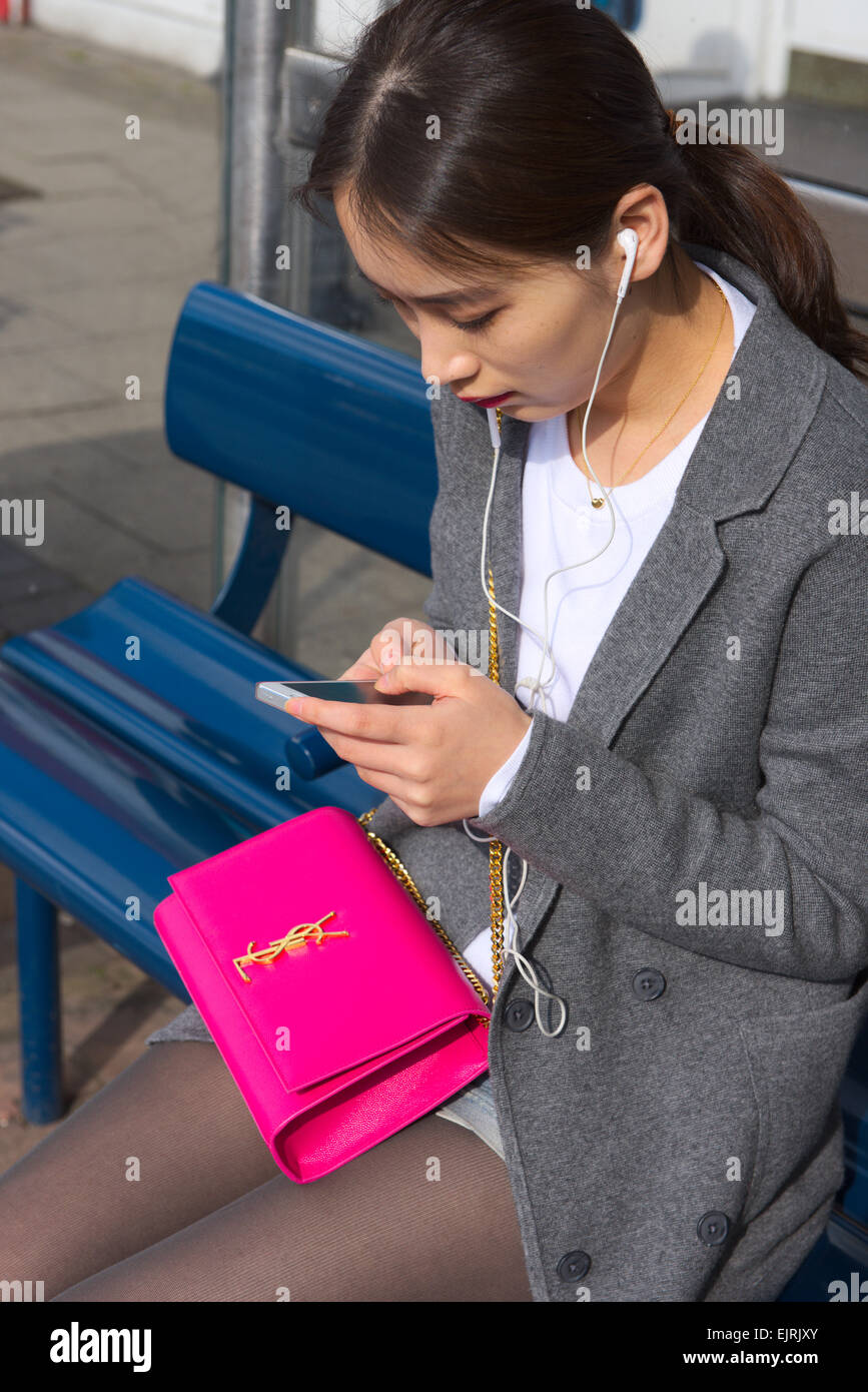Attraktive junge Frau sitzt auf der Bank SMS auf Handy Stockfoto