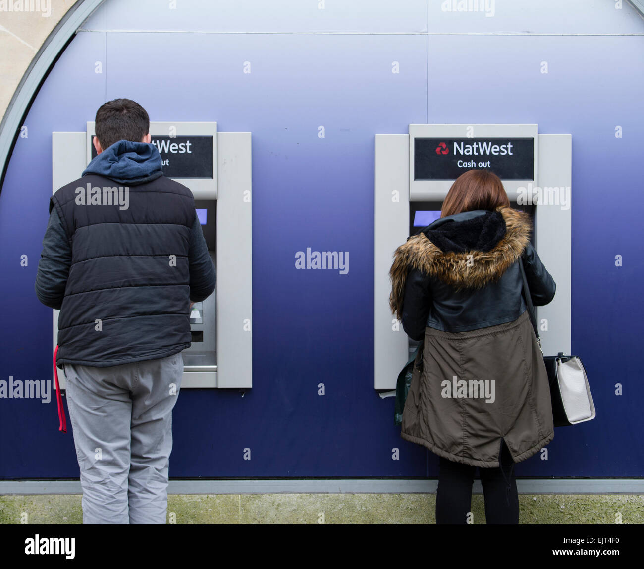 Zwei junge Menschen, die mit NatWest National Westminster Bank Geldautomaten Bargeld zeigen Maschinen, Swansea Wales UK Stockfoto