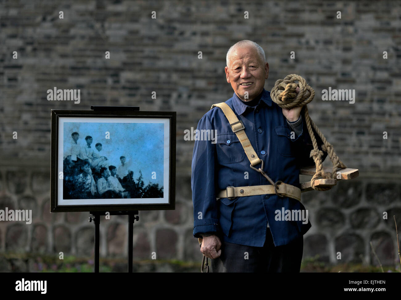 (150401)--SHUCHENG, 1. April 2015 (Xinhua)--Luo Qinzhong, 77, posiert für ein Foto neben einem Gruppenfoto in 1959 zeigt Mitglieder des Power Supply-Team für den Aufbau Longhekou Reservoir in Shucheng County, der ostchinesischen Provinz Anhui, 29. März 2015 getroffen. Luo Qinzhong, ein Absolvent der Shucheng Wasser Conservancy College, war ein Monitor ein Power-Supply-Team beim Aufbau Longhekou Reservior. Er war der dritte Mensch in der hinteren Reihe in das Bild, das im Jahr 1959. Longhekou Reservoir, welches eine Speicher-Kapazität von 903 Millionen Kubikmeter hat, wurde 1958 durch die gemeinsamen Anstrengungen am Fluss Hangbu gebaut. Stockfoto