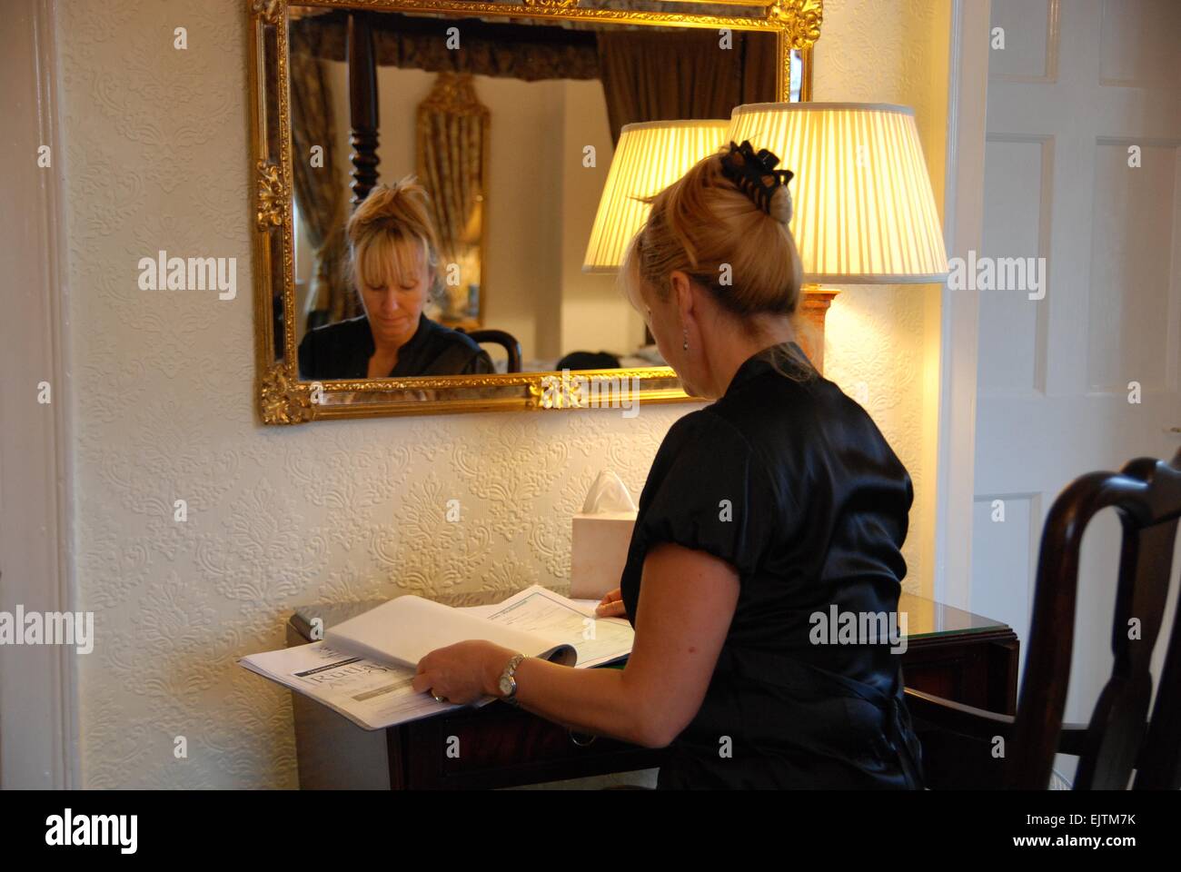 Frau im Hotelzimmer, die die Hotelinformationen gelesen hat Vorderseite eines Spiegels neben einer Lampe nach der Überprüfung Zoll Stockfoto