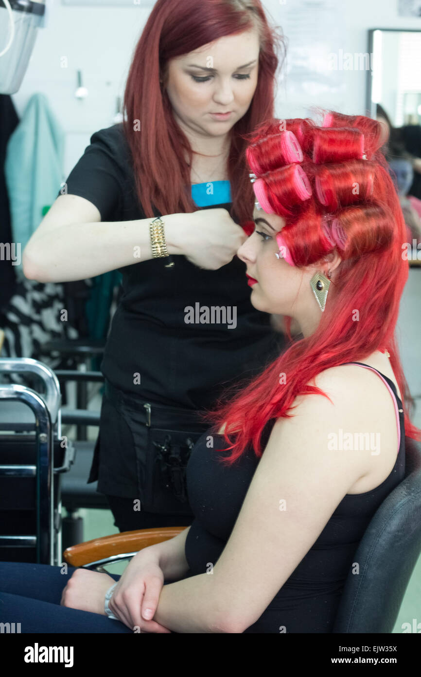 Aufrechte eines weiblichen Salon Arbeitnehmers Someones Haare mit Lockenwicklern, Haarverlängerungen und leuchtend roten Haaren zu tun. Stockfoto