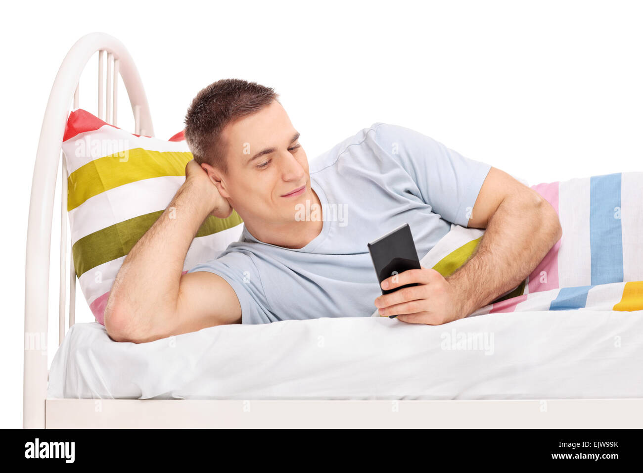 Studioaufnahme von einem entspannten jungen Mann in einem Bett liegen und Surfen im Internet auf seinem Handy isoliert auf weißem Hintergrund Stockfoto
