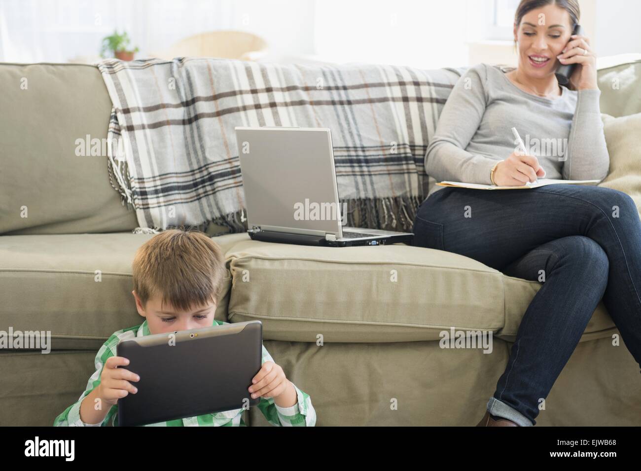 Mutter und Sohn (6-7) sitzen im Wohnzimmer mit Tablet und Notebook Stockfoto