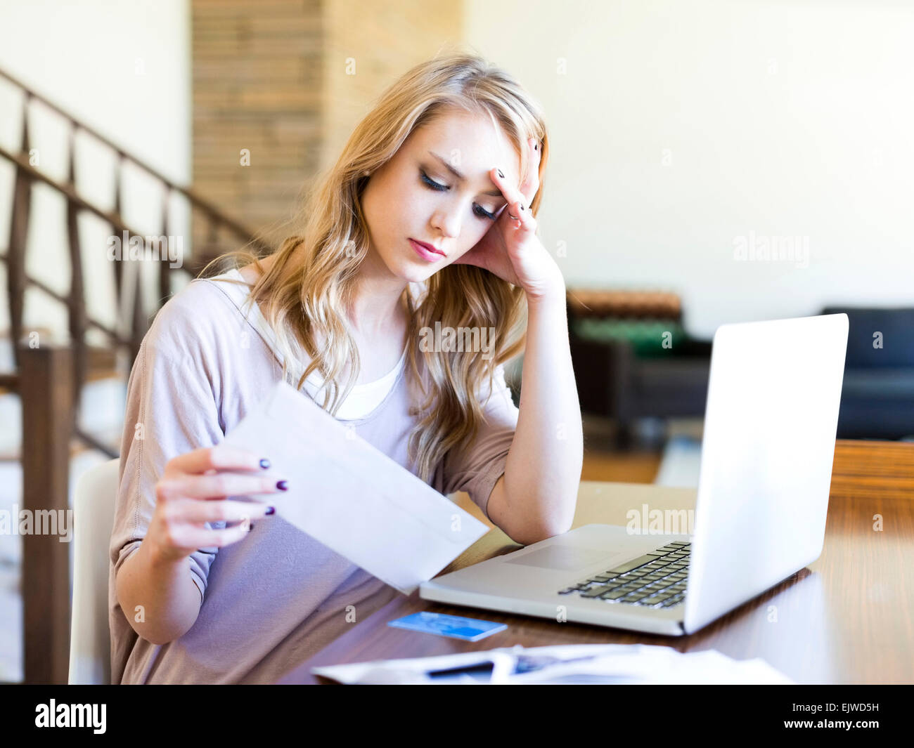 Junge Frau mit Laptop Blick auf Papier-Rechnung am Tisch sitzen Stockfoto