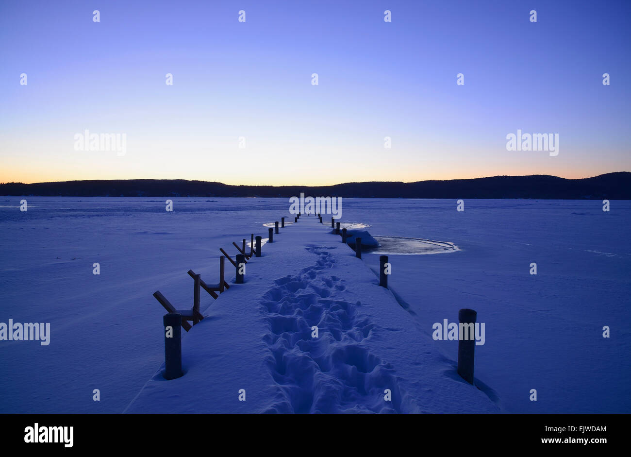 Symmetrische Bild des verschneiten Steg mit Spuren im Morgengrauen, Hügeln am Horizont, Lake George, New York, USA Stockfoto