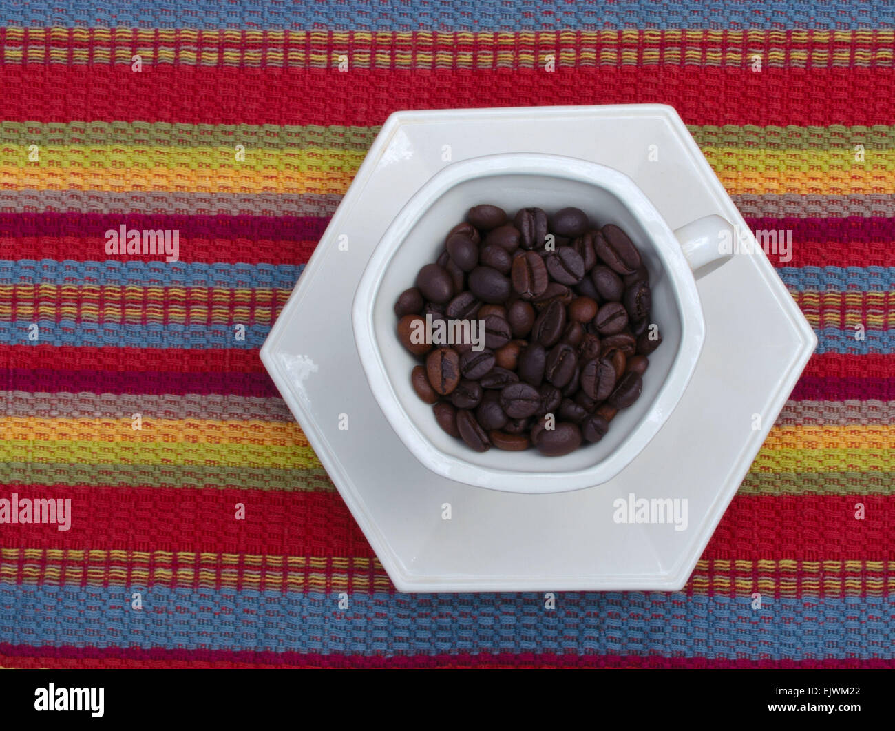 Dunkle Röstung der Kaffeebohnen in eine Kaffeetasse auf einer bunten Tischset Stockfoto