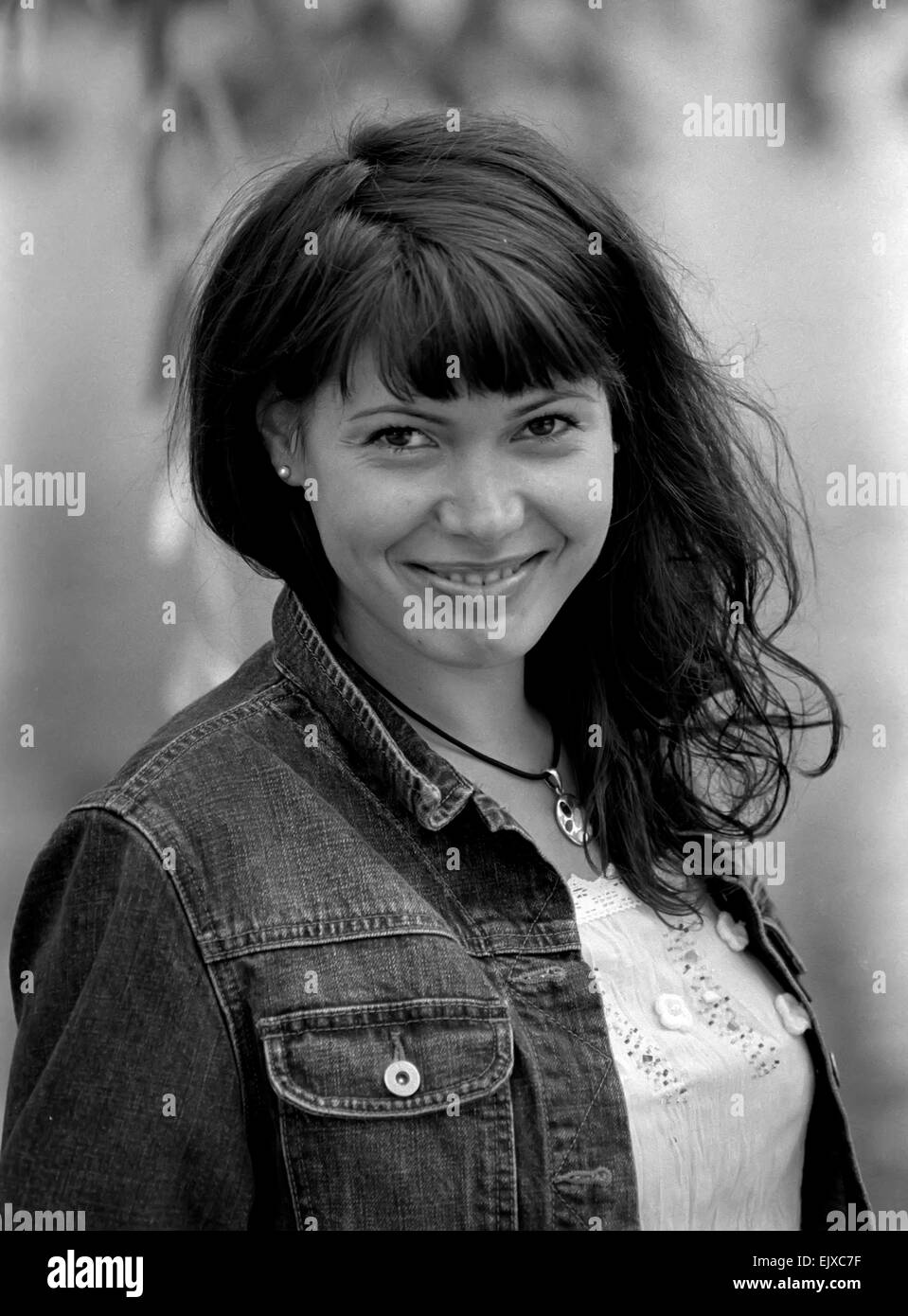 Schwarz-weiß-Porträt einer lächelnden jungen Frau in Jeans Jacke und mit rundem Anhänger. Stockfoto