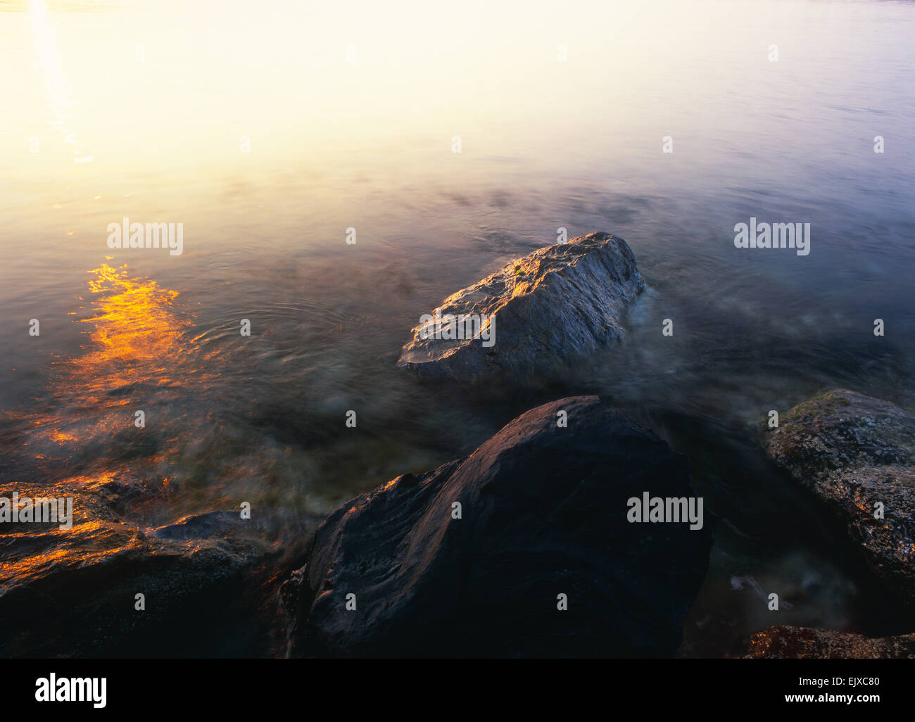 Lange Belichtung medium format Marine der Felsen im Wasser milchig und orange Reflexionen der aufgehenden Sonne. Stockfoto