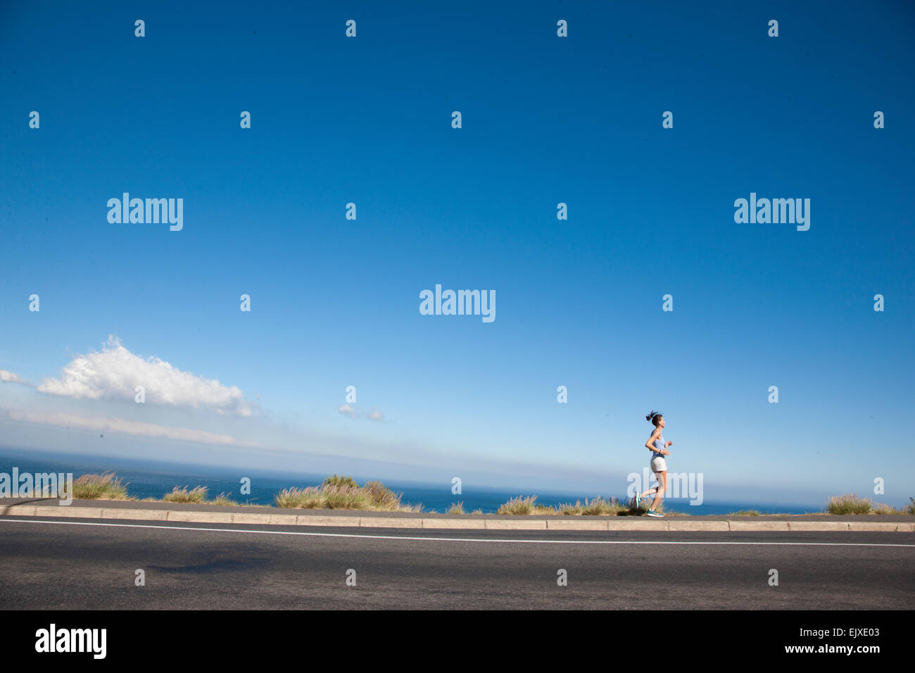 Frau läuft auf asphaltierten Straße vom Ozean Stockfoto
