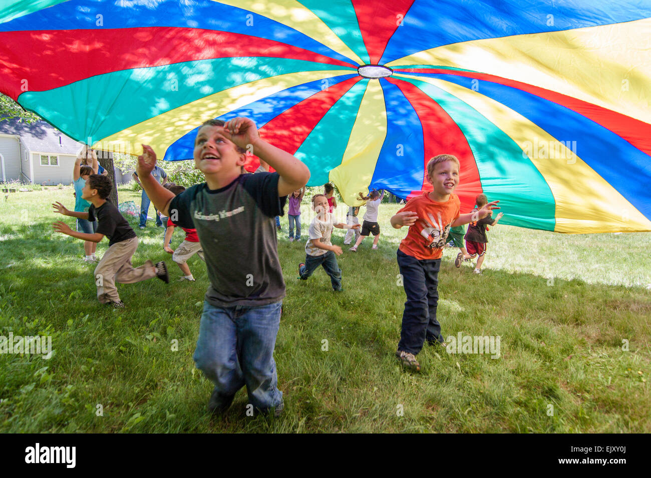 Jungen und Mädchen spielen unter einem bunten Fallschirm Stockfoto