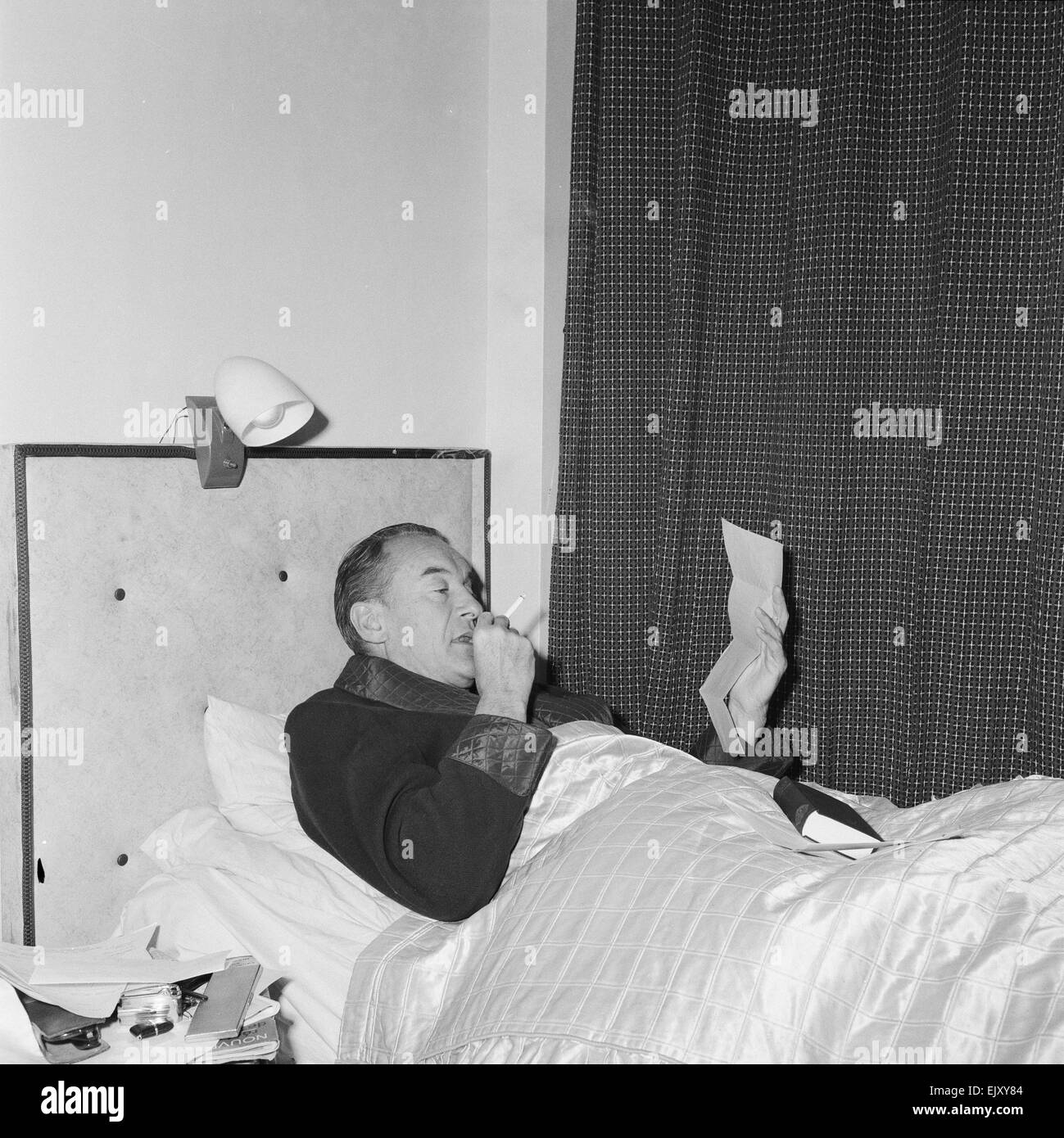 Schauspieler George Sanders setzt sich in seinem provisorischen Bett in Elstree Studios, wo er derzeit "Blaubärten zehn Flitterwochen", 7. November 1959 filmt.    Der Film basiert auf den realen Verbrechen des französischen Serienmörders Henri Landru.      Lokalen Caption *** Rauchen im Bett Stockfoto
