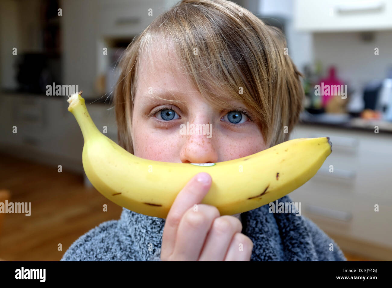 ein Kind hält eine Banane, einen grüner Saft Smoothie für ein gesundes Frühstück zu machen bereit Stockfoto