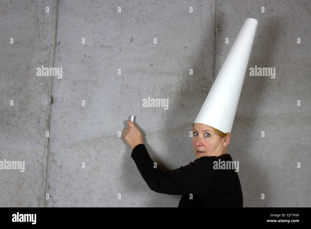 Frau trägt eine Dunce Cap mit Kreide auf eine Betonwand Stockfoto