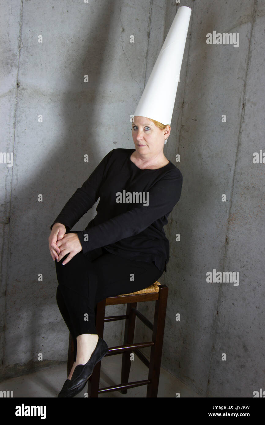Frau trägt eine Dunce Cap auf Hocker in der Ecke sitzen Stockfoto