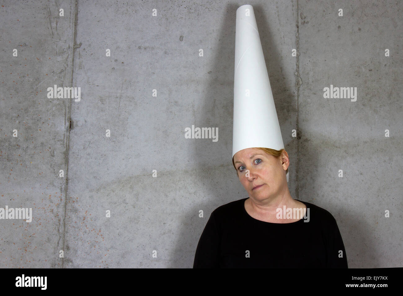 Frau trägt ein Dunce Cap steht gegen eine Betonwand Stockfoto