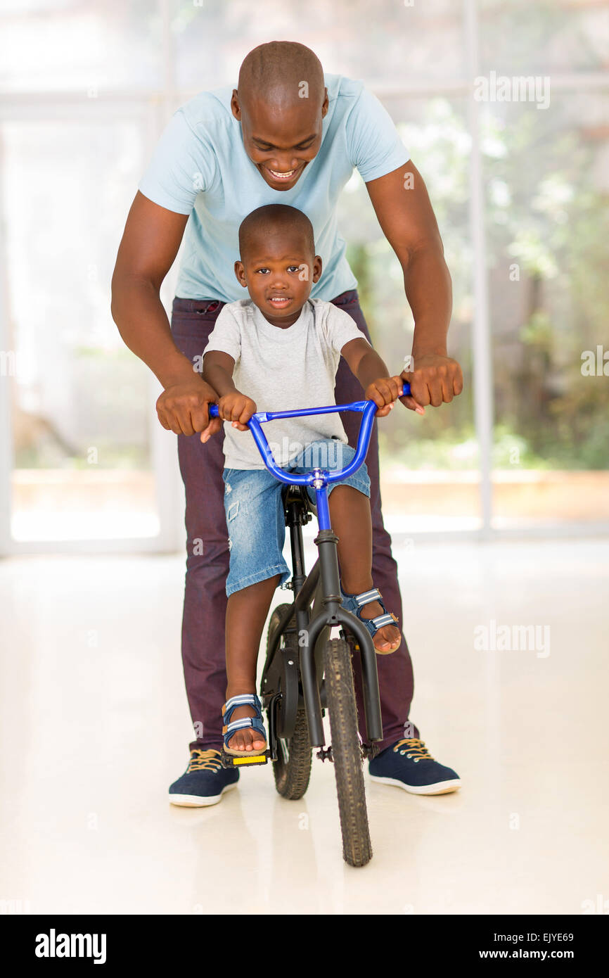 glücklich afrikanischen Mann helfen, sein Sohn, mit dem Fahrrad im Innenbereich Stockfoto
