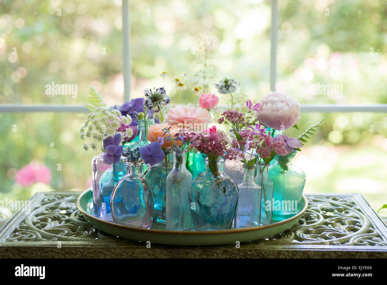 Blumenarrangement von Schnittblumen in blauen Flaschen einschließlich Rosen, Hortensien, Pfingstrosen, Schafgarbe, Mutterkraut und Queen Anne es Lace Stockfoto