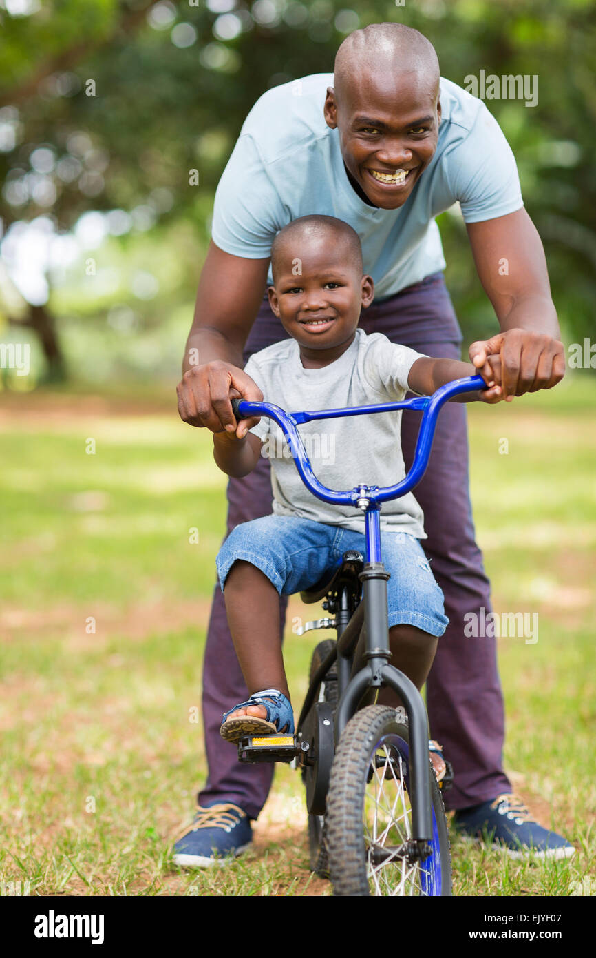 liebevolle afrikanischen Vaters Sohn eine Radtour im Freien zu helfen Stockfoto