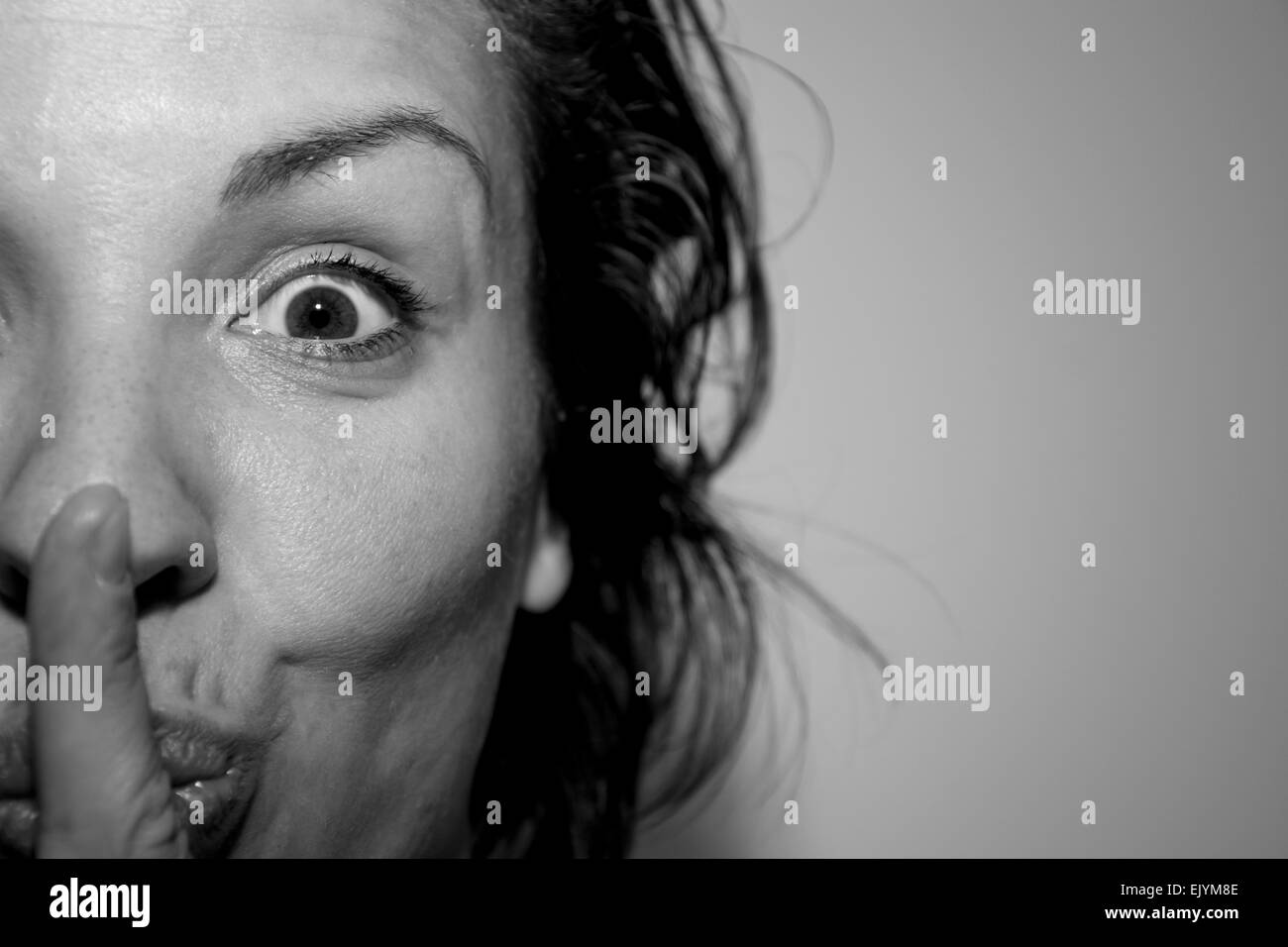 Porträt einer hübschen jungen Frau zeigt Stille mit Finger in Monochrom drinnen hautnah Stockfoto