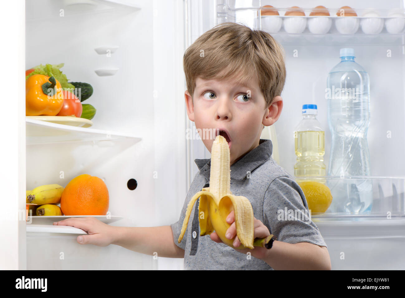 Kleiner Junge Banane in der Nähe von offenen Kühlschrank Essen Stockfoto