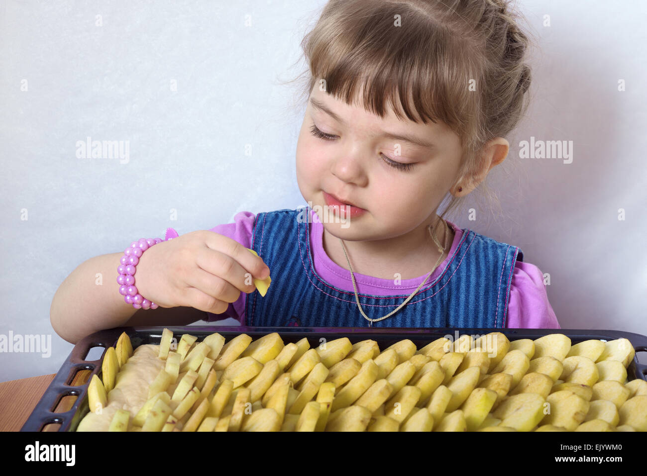 Vierjährige Mädchen bringt Apfelscheiben in Apfelkuchen Stockfoto