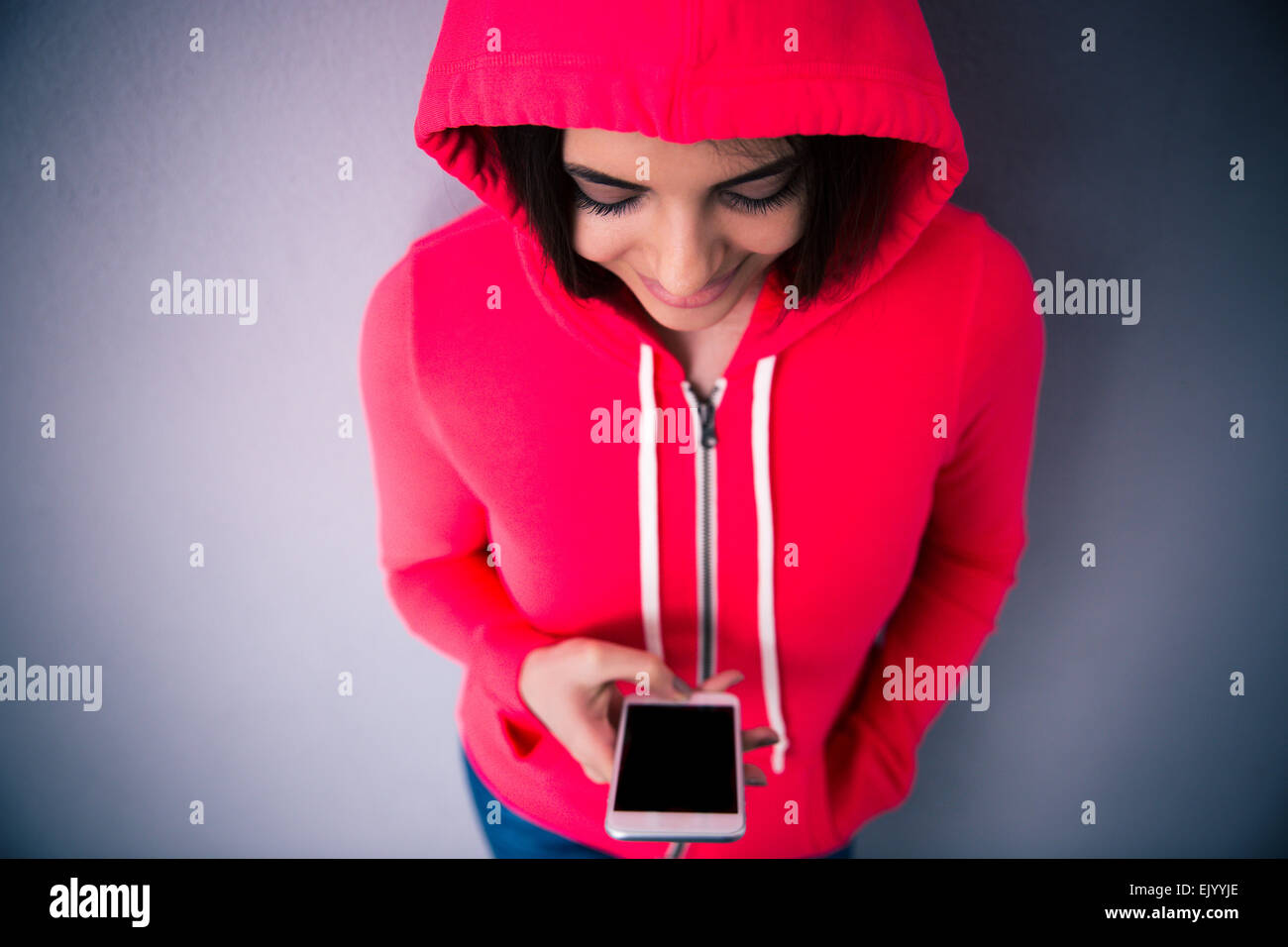 Glückliche Frau Smartphone über grauen Hintergrund zu halten. In rosa Sakko tragen. Auf der Suche auf smartphone Stockfoto