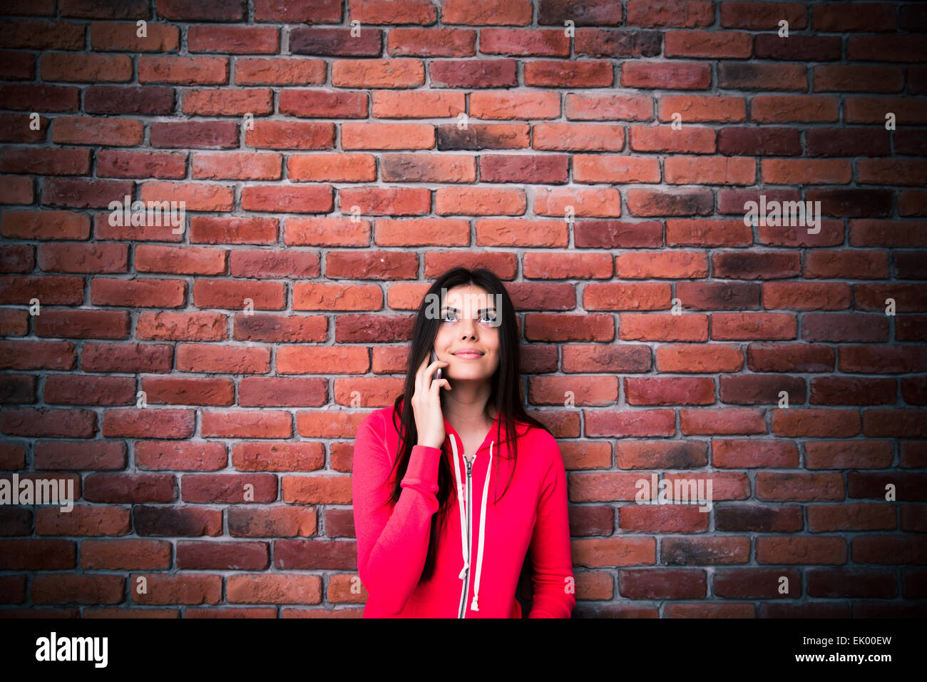 Junge Frau am Telefon sprechen und blickte zu Exemplar über Rocko Mauer. Sport Jacke Stockfoto