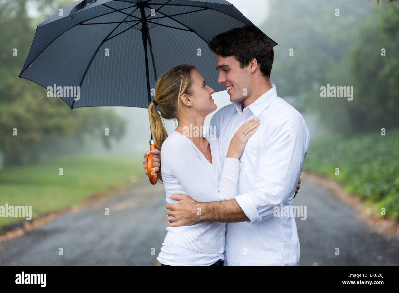 junges Liebespaar mit Schirm im Regen Stockfoto