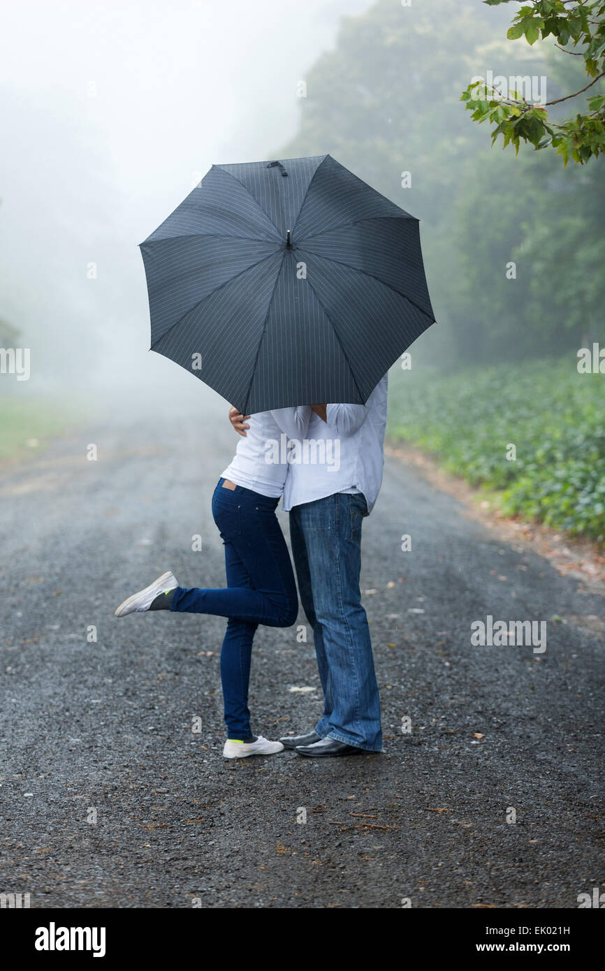 romantische Pärchen versteckt sich hinter dem Schirm im Regen Stockfoto