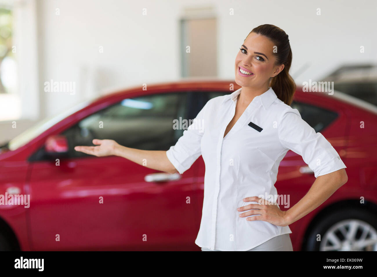 glückliche junge Verkäuferin, die einladende Geste im Autohaus Stockfoto