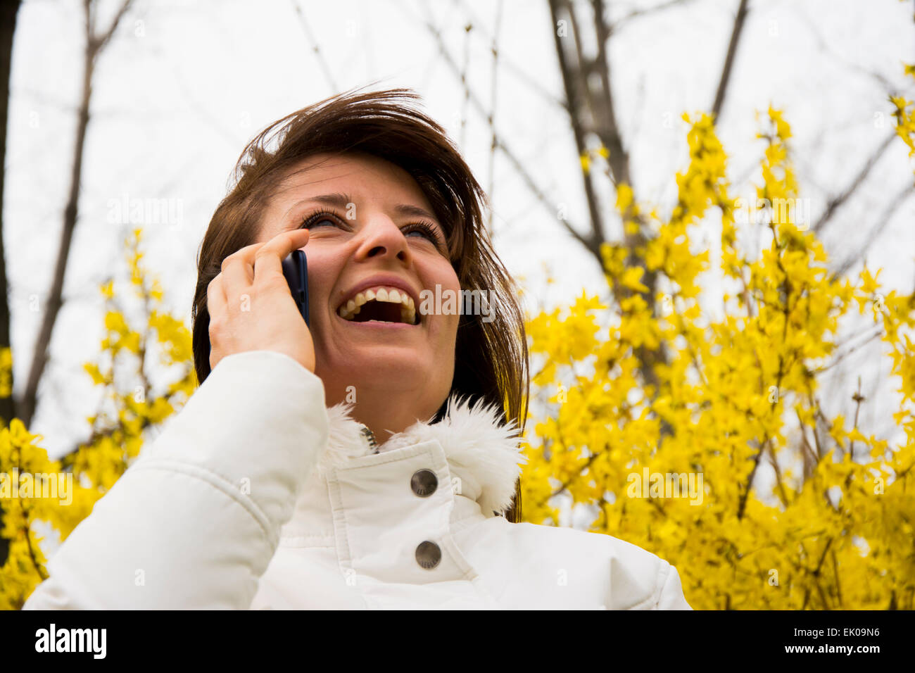 Hübsche junge Frau lächelt während des Gesprächs am Telefon. Sie lächelt wie sie mit ihren Freunden im Frühjahr blühen kommuniziert. Stockfoto