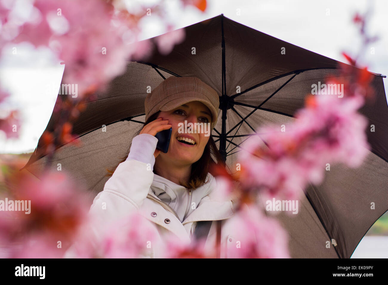 Hübsche junge Frau lächelt während des Gesprächs am Telefon. Sie lächelt wie sie mit ihren Freunden im Frühjahr blühen kommuniziert. Stockfoto