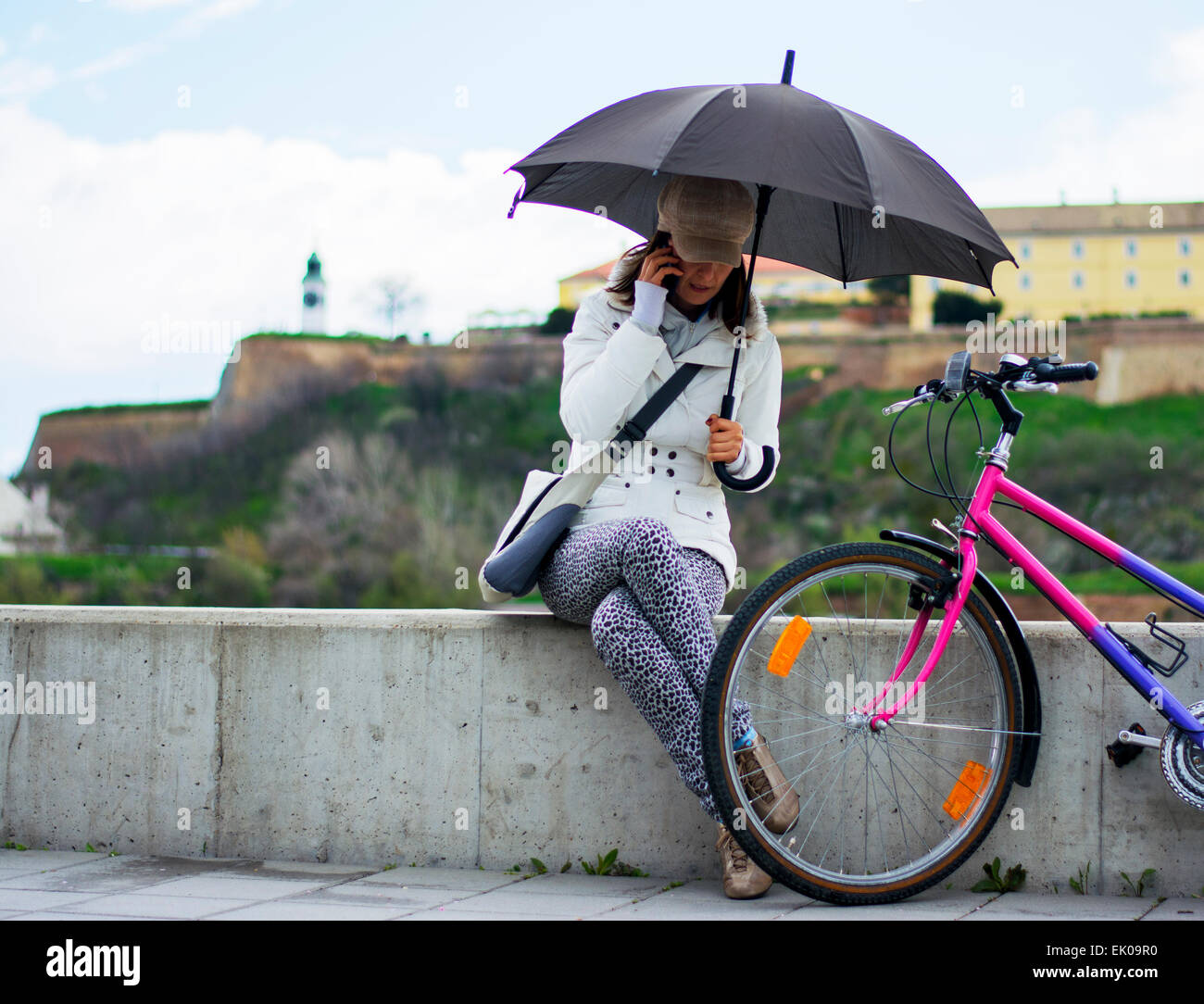 Hübsche junge Frau mit Fahrrad neben telefonieren. Sie lächelt wie sie kommuniziert mit ihren Freunden mit Festung ich Stockfoto