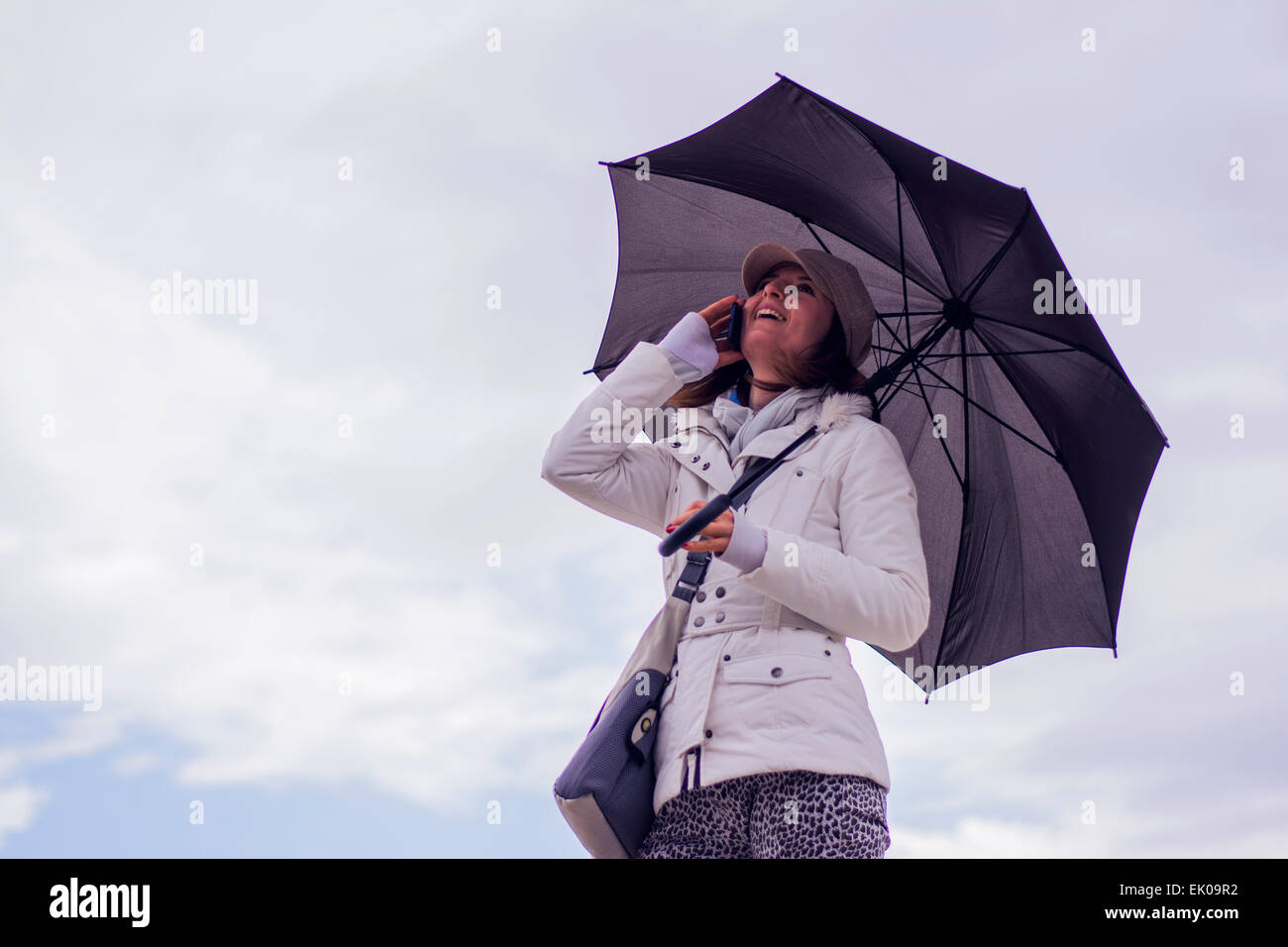 Hübsche junge Frau unter Dach Lächeln auf den Lippen und am Telefon zu sprechen. Sie lächelt wie sie mit ihren Freunden kommuniziert. Stockfoto