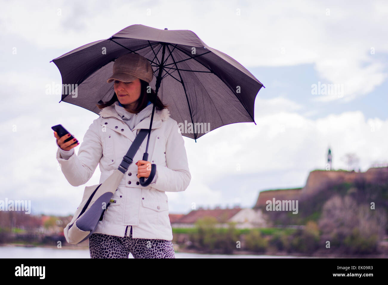 Hübsche junge Frau mit Hut unter Dach auf dem Handy eingeben. Sie lächelt wie sie mit ihren Freunden mit Fort kommuniziert Stockfoto