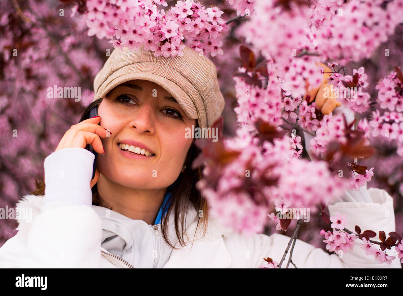 Hübsche junge Frau lächelt während des Gesprächs am Telefon. Sie lächelt wie sie mit ihren Freunden im Frühjahr blühen kommuniziert. Stockfoto